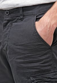 Pantalones negros con una textura suave, que cuentan con bolsillos laterales y un cierre de botón en la cintura. La tela parece ligeramente arrugada.
