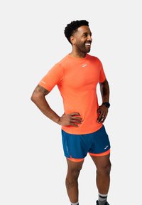 Ropa activa para hombres: camiseta de manga corta de color naranja brillante con detalles reflectantes, combinada con pantalones cortos azules que tienen acentos naranjas y textura de malla.