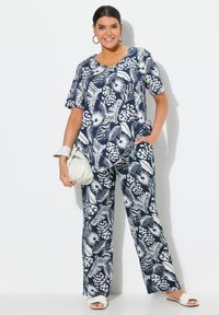 Ensemble top et pantalon à motifs floraux bleu marine, présentant une coupe décontractée, des manches courtes et des poches latérales discrètes. Accessoirisé avec un sac léger.