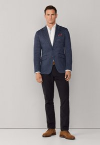 Marineblauwe blazer met structuur en neklapel met inkeping, twee voorzakken, gecombineerd met een wit overhemd en donkere broek, aangevuld met bruine suède schoenen.