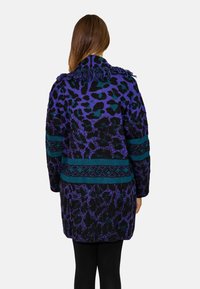 Cappotto lavorato a maglia in stampa animale viola e teal con colletto con frange e bande decorative. Maniche lunghe, vestibilità comoda, superficie testurizzata.