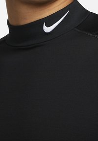 Nahaufnahme einer Person, die ein schwarzes Sportoberteil mit hohem Kragen und einem weißen Nike-Swoosh-Logo am Kragen trägt.