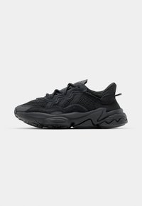 Zapatillas negras con parte superior de malla, acentos texturizados y una suela de goma gruesa con un patrón en zigzag. Incluye cordones y un cuello acolchado.