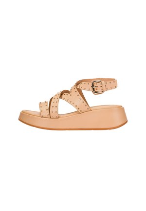 Sandalia de plataforma beige con tiras cruzadas adornadas con tachuelas, hebilla ajustable en el tobillo y suela gruesa, sobre fondo blanco.