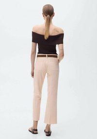 Haut marron décolleté, pantalon rose clair ajusté avec ourlets effilochés, complété par des sandales à lanières marron, présentant une silhouette moderne et épurée.