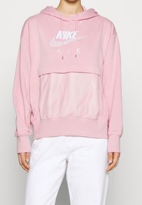 Ljusrosa Nike sweatshirt med ett nätpanel, oversized passform, hoodie, dragskor och vit logotryck "NIKE AIR" framtill.