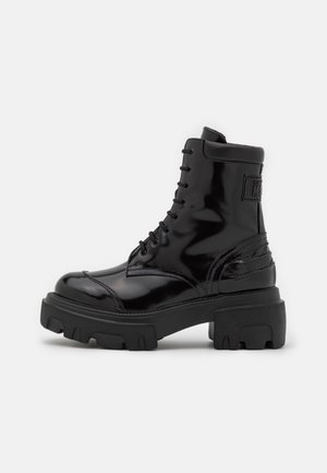Botte de combat noire en cuir brillant à lacets, semelle épaisse à crampons et col rembourré à la cheville, vue de côté.