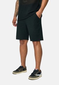 Shorts en coton noir avec une coupe décontractée, dotés de poches latérales. Assortis à des baskets noires et beiges. Le haut est en maille texturée.