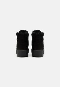 Botas de tobillo de ante negro con cuello de piel negra esponjosa, suela de goma texturizada y diseño minimalista. Sin herrajes ni patrones visibles.