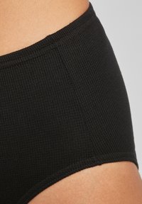 Melnas ribotas auduma apakšbikses ar mīkstu elastīgu jostasvietu, kurām ir bezšuvju mala un gluda tekstūra, izstrādātas ērtībai un piemērotībai.