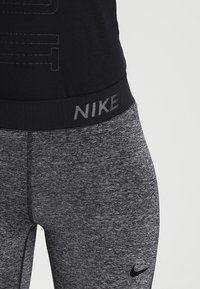 Szare legginsy sportowe z teksturowanym wykończeniem, z szerokim czarnym pasem w talii z logo "NIKE" w odblaskowym nadruku.