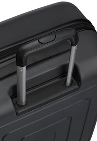 Valise rigide noire avec poignée télescopique argentée prolongée et fermeture éclair supérieure.