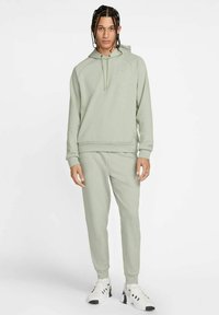 Light green sweatshirt with an adjustable hood and ribbed cuffs, paired with matching sweatpants. White and black athletic shoes complete the outfit.