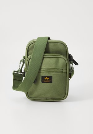 Borsa a tracolla verde in tessuto con cinghia regolabile, tasca frontale con zip e patch con logo nero. Materiale testurizzato con cuciture rinforzate.