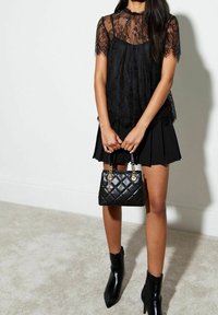 Black lace top with short sleeves over a black pleated skirt. Accessories include a quilted black handbag and shiny black ankle boots.