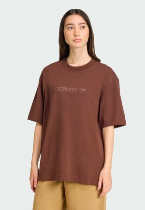 Brązowy, oversize'owy t-shirt wykonany z bawełny, z okrągłym dekoltem i krótkimi rękawami. Z przodu umieszczone jest wytłoczone logo adidas.