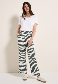 Witte t-shirt gecombineerd met wijde groene en witte gestreepte broek. De broek heeft een elastische taille en zijzakken. Casual schoenen maken de outfit af.