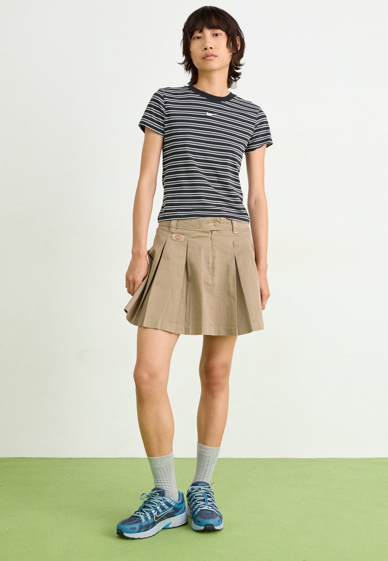 Gestreiftes T-Shirt mit kurzen Ärmeln in Schwarz und Weiß, khakifarbenen Faltenrock, grauen Socken und blauen Sportschuhen. Minimalistisches Design, lässiger Stil.