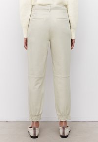 Ljust beige elastiska byxor med smidig textur, två bakfickor och knä detaljer, tillsammans med ljusa skor.
