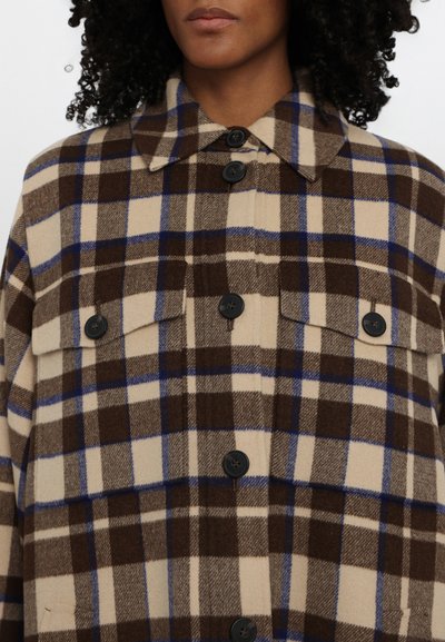 Chaqueta de cuadros de gran tamaño en marrón y beige con acentos en azul, que presenta un cuello, cierre de botones y dos bolsillos en el pecho. Tejido suave y texturizado.
