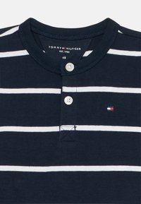 Camicetta a maniche corte a strisce blu navy con strisce bianche, dotata di un collo henley con bottoni e un piccolo logo ricamato sul petto.