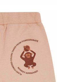 Helle rosa Baumwollhosen mit einem braunen Affen-Graphic, der einen Granatapfel hält. Der Text lautet: "Pflanzenbasierte Farben, entnommen aus Granatapfel!"