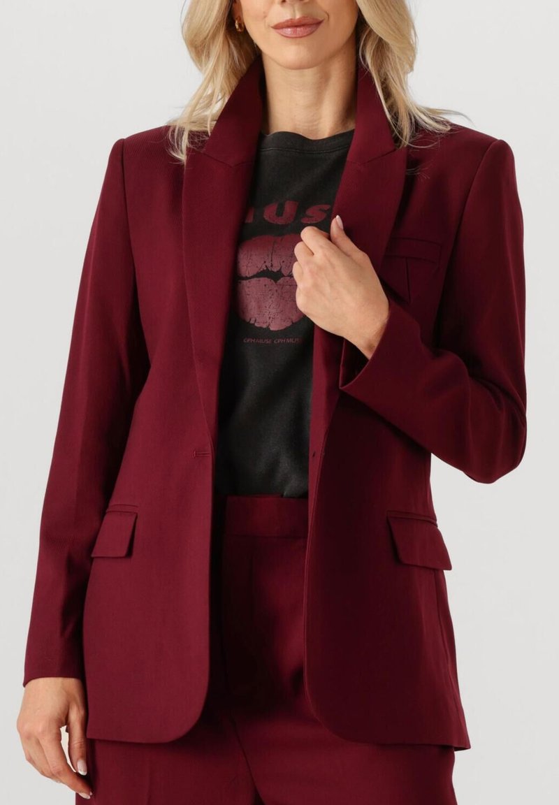 Maroon tailored blazer with a notched collar, two front pockets, and a fitted silhouette, layered over a black graphic T-shirt.
