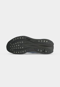 Semelle en caoutchouc noire d'une chaussure de course avec des motifs de bande de roulement profonds et un petit logo Puma près du talon.
