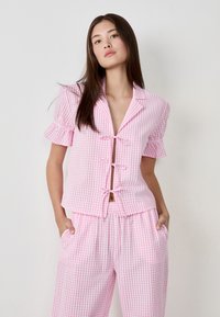 Pink and white gingham two-piece outfit featuring a cropped button-up shirt with ruffled sleeves and matching wide-leg pants with an elastic waistband.