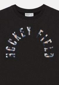 T-shirt de algodão preta com a inscrição "Hockey Field" em impressão camuflada multicolorida, design curvado e gola redonda ribbed.