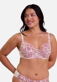 Bralette en dentelle florale crème avec des motifs roses, violets et verts ; dispose de bretelles réglables et d'un détail de bouton décoratif central.