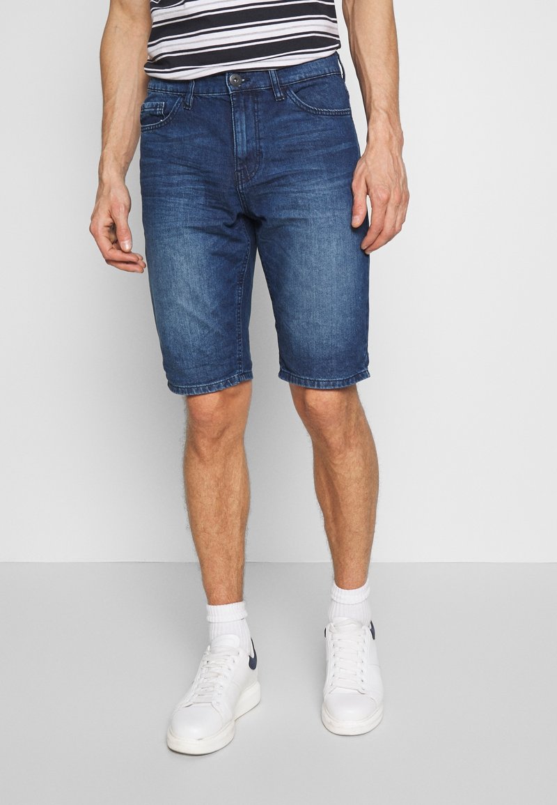 Shorts in denim di color blu scuro con un classico design a cinque tasche, orli piegati e un leggero effetto sbiadito. Abbinati a sneakers bianche sportive.