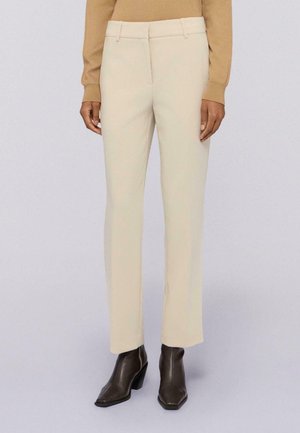 Pantaloni beige su misura con design a gamba dritta e tasche frontali, realizzati in un tessuto liscio. Abbinati a stivaletti con tacco scuro.
