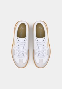 Pair of white and beige Puma sneakers with gum soles, laces tied, viewed from above on plain light background.