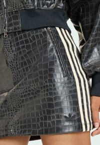 Černá minisukně z umělé kůže s krokodýlím vzorem, bílými třípruhovými akcenty a bočním zipem s logem Adidas.