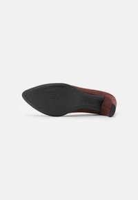 Scarpa con tacco alto in suede rosso, con una superficie liscia, caratterizzata da una punta affusolata e una suola in gomma con una presa a motivo.