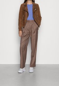 Brun mocka motorcykeljacka över en blå skjorta, kombinerad med högmidjade randiga byxor och ljusa sneakers.