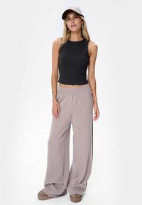 Zwarte aansluitende tanktop met wijde lichtgrijze sweatpants. De broek heeft een relaxte pasvorm, een zachte textuur en een geribde tailleband. Een grijze pet maakt de look compleet.