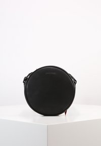 Borsa rotonda in pelle nera con finitura liscia, tracolla e dettagli del logo impresso. Design minimalista e forma compatta.