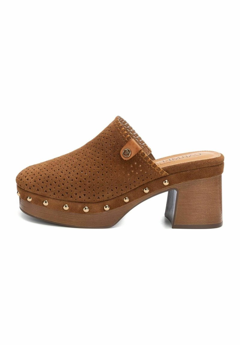 Zoccolo in suede marrone con design perforato, dettagli in metallo dorato lungo la base e un tacco in legno spesso. Presenta un dettaglio a forma di bottone decorativo.