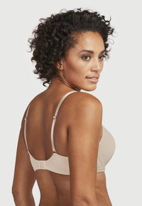 Beige draadloze bh met verstelbare bandjes, gladde textuur, haak-en-oogsluiting en een eenvoudig ontwerp voor ondersteuning en comfort.