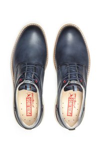 Zapatos de cuero azul marino con punta redonda, parte delantera con cordones, costuras en contraste y ojales rojos. Marca Pikolinos en la plantilla.