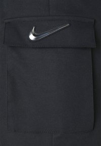 Svart tyg med en slät textur som har en framficka och en silverfärgad Nike-logotyp på ficklocket.