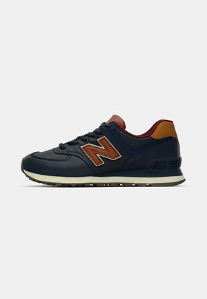 Marineblauwe en bruine New Balance sneaker met witte zool, vetersluiting aan de voorkant en een reliëflogo op de zijkant en hiel.