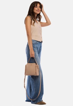Borsa in pelle beige con texture trapuntata, doppio manico e tracolla regolabile, abbinata a un gilet beige chiaro e jeans a gamba larga.