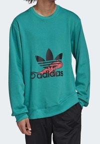 Tiffanysin värinen crewneck-sweater, jossa on musta ja punainen Adidas-logo, jossa on abstrakti muotoilu. Ribbärit hihansuissa ja helmassa, pehmeä kangastekstuuri.