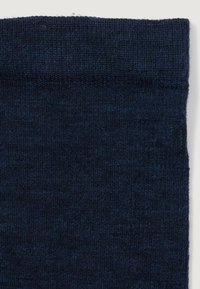Primer plano de una tela de punto azul oscuro con costuras finas visibles y ligera variación en la textura a lo largo de los bordes.