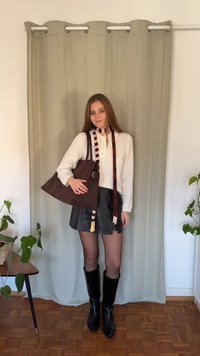 Bolso marrón de hombro, top blanco de manga larga, minifalda negra de cuero, botas negras hasta la rodilla y bufanda de rayas multicolor.