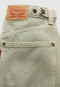 Πίσω τσέπη σε ανοιχτό μπεζ τζιν Levi's με ραμμένες λεπτομέρειες, μεταλλικά καρφιά, θηλιά για ζώνη και καφέ δερμάτινη ετικέτα Levi Strauss & Co.