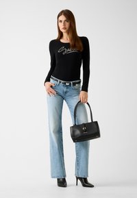 Schwarzes langärmeliges Oberteil mit silbernem Logo, hellblaue hochtaillierte Jeans, schwarze Stiefeletten mit Absatz und eine kleine schwarze Handtasche mit goldenen Akzenten.